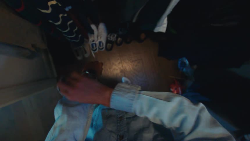 A person is getting dressed inside a closet securing a metalbanded wristwatch and then bends down to select and put on a pair of black sneakers from the wooden floor