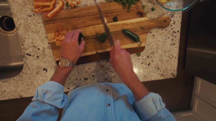 A person in a denim shirt slicing a jalapeo on a wooden cutting board