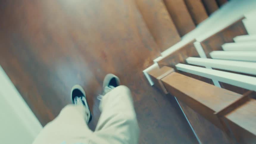 Man holds the banister while walking down a wooden staircase at home