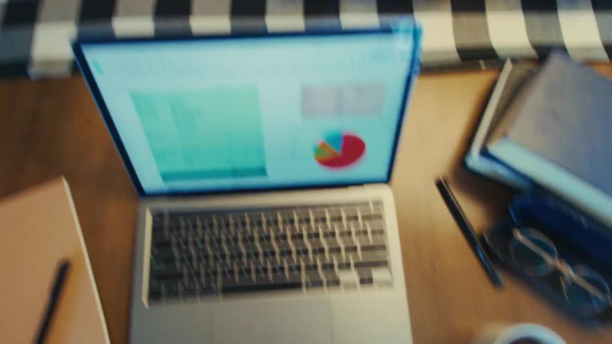A person carrying a mug of coffee sitting in front of a laptop and then opening a book