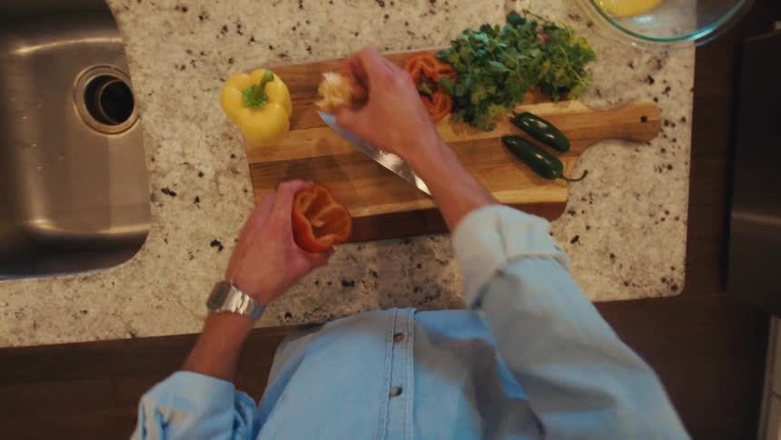 Man standing in his kitchen slices a bell pepper while preparing an egg dish