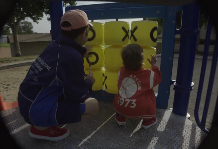 A young boy and a toddler play joyfully with a rotary toy in the playground at midday enjoying their time together