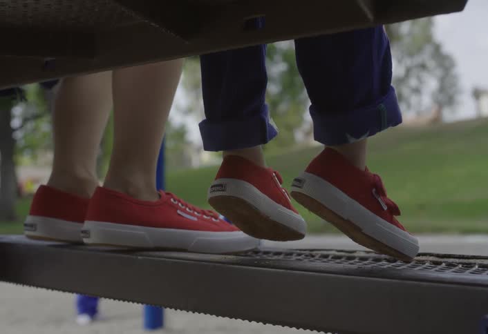The legs of an adult and a child wearing red shoes while sitting on a bench