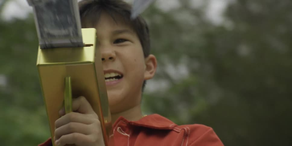 Child holding a toy that shoots ribbon in a wooded area