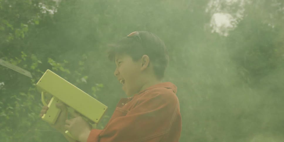 The first clip shows a young boy wearing a striped cap and a green and white jacket emerging from behind a large green bush and trimming it with redhandled shears the other two clips show the same boy outdoors wearing a red jacket and gold chain hol