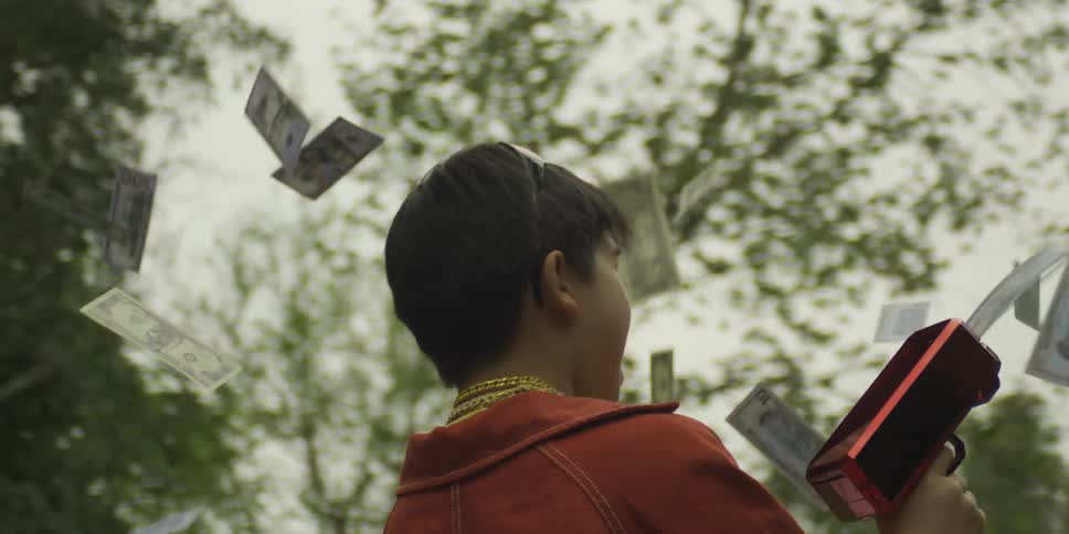 A young boy uses a money gun as cash flies through the air outdoors