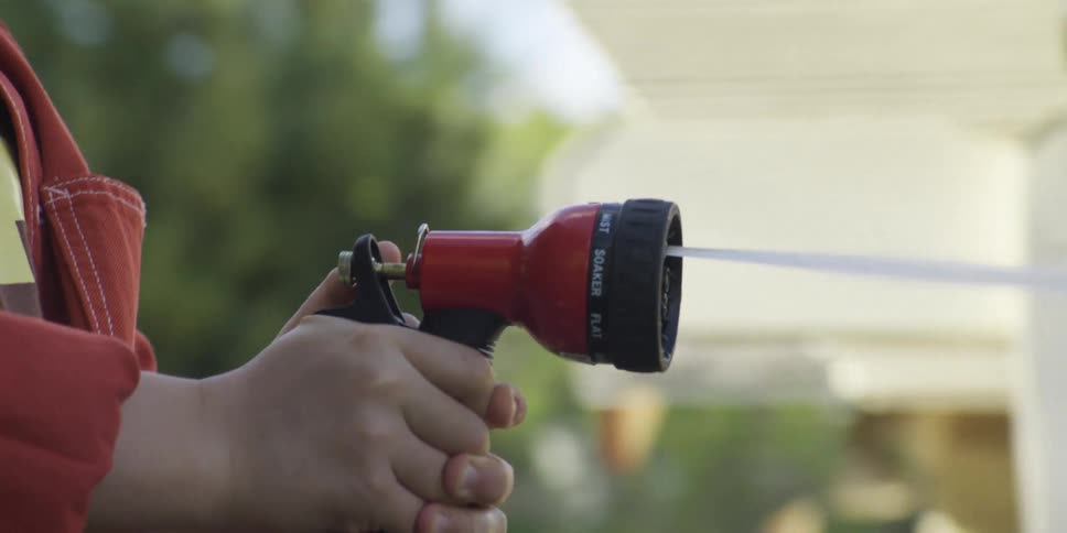 A persons hand holding a red hose while spraying water forward