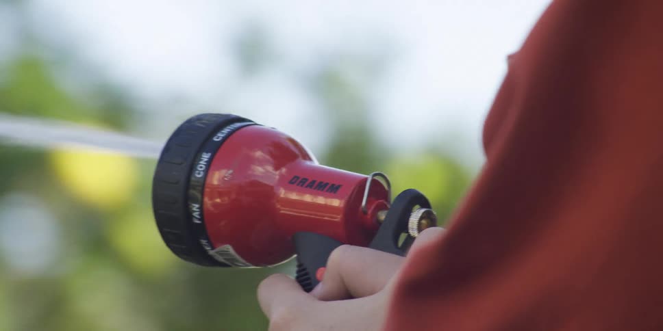 Closeup of a boy spraying water from a red dramm garden hose nozzle outdoors