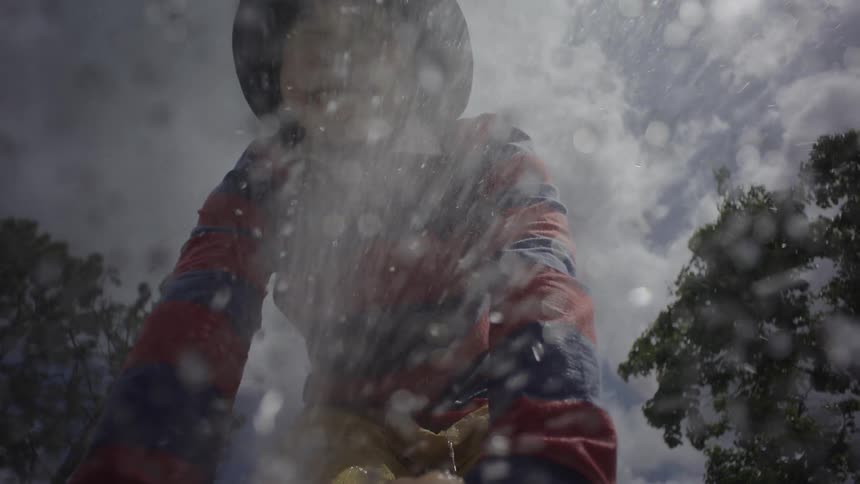 A young boy in a hat and striped shirt laughing as he is sprayed with water