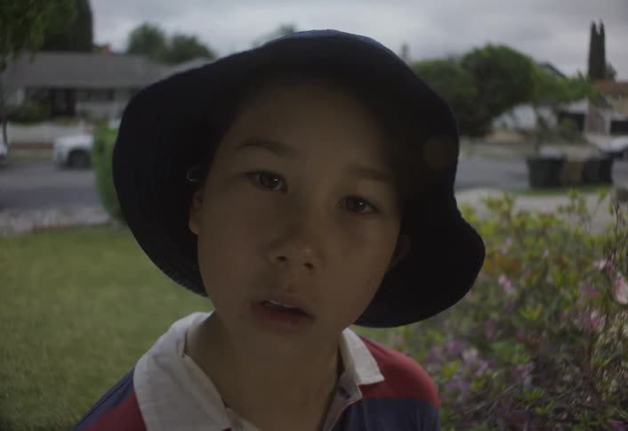 A young boy looks toward the camera with a suspenseful expression in a suburban yard