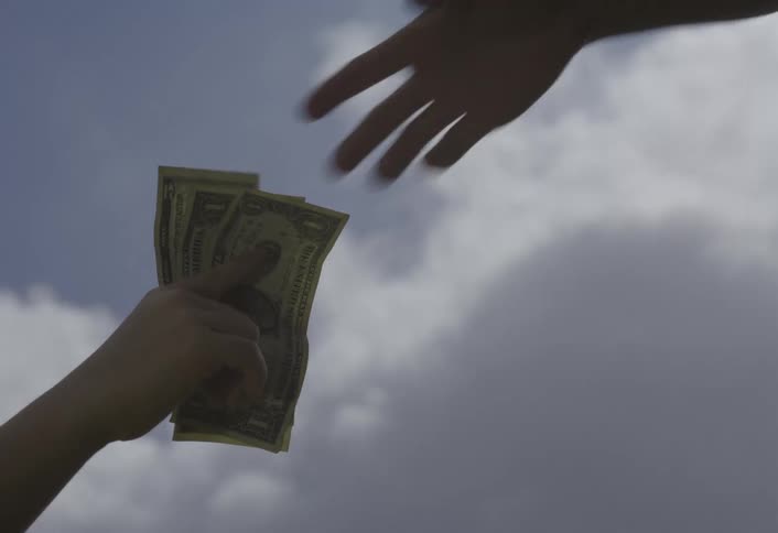 Against a bright cloudy sky two silhouetted hands exchange a small stack of paper currency in a brief closeup financial transaction