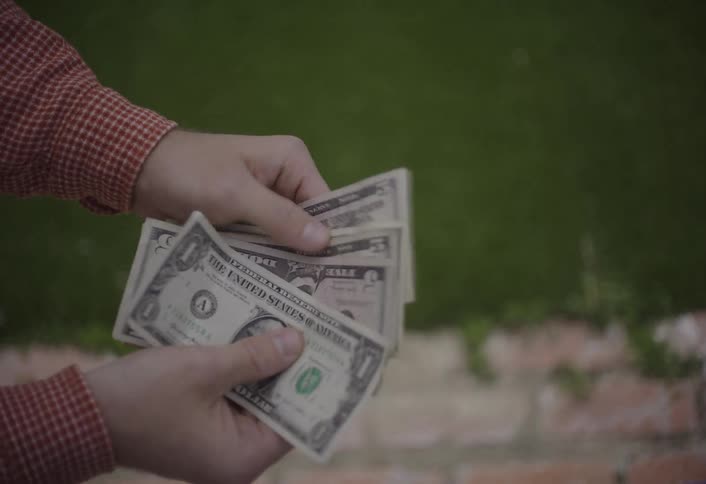 Closeup of two hands exchanging a small stack of dollar bills outdoors