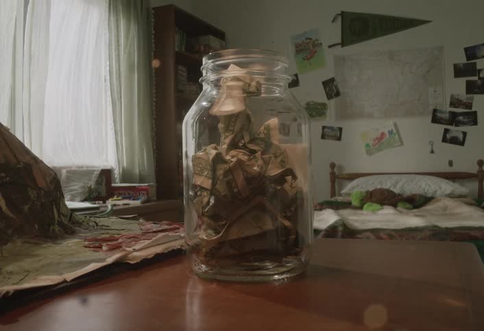 Glass jar being filled with banknotes on a table in a childs bedroom