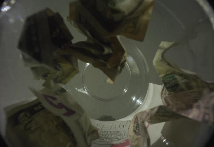 Captured from a lowangle inside a clear container a boys hand deposits several crumpled dollar bills with the face briefly seen looking down into the jars opening
