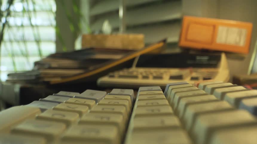 Closeup of a computer keyboard with blurred books and office supplies in the background