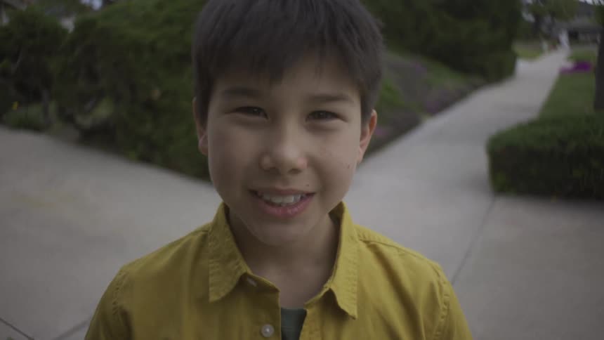 The face of a young boy wearing a yellow shirt looking ahead and smiling