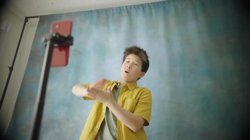 The boy is doing poses in front of the cell phone camera