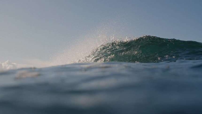 A wave curls and crashes upon the surface the ocean on a sunny day