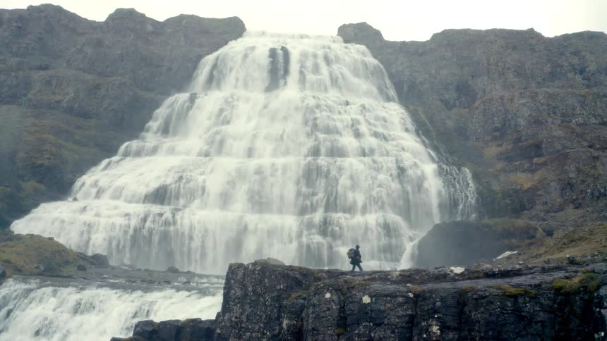 Hiker walking on a plateau next to a massive waterfall outdoors during day time