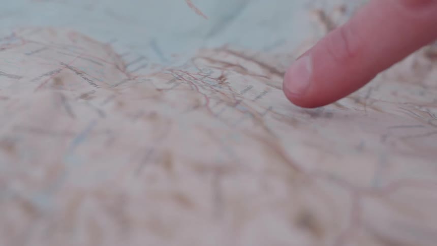 A persons finger pointing at a map route at midday