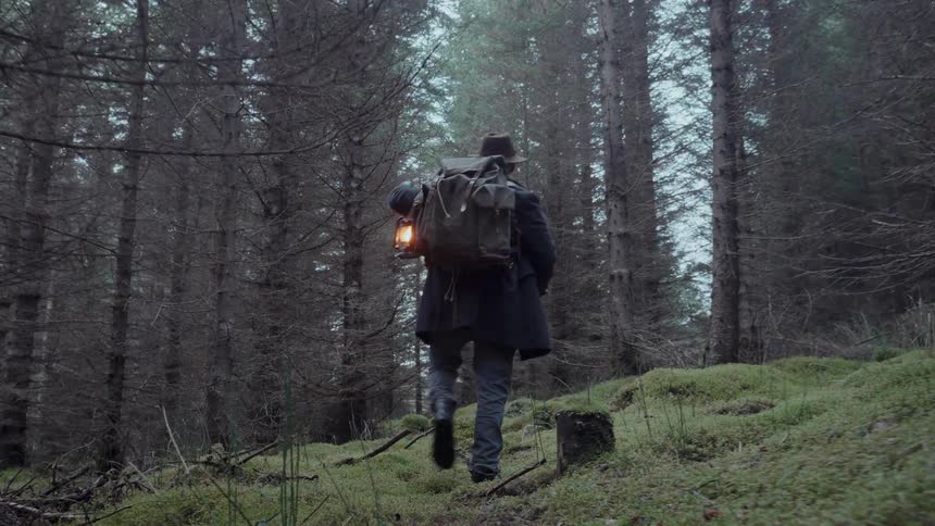 Hiker walking into the woods carrying a lantern