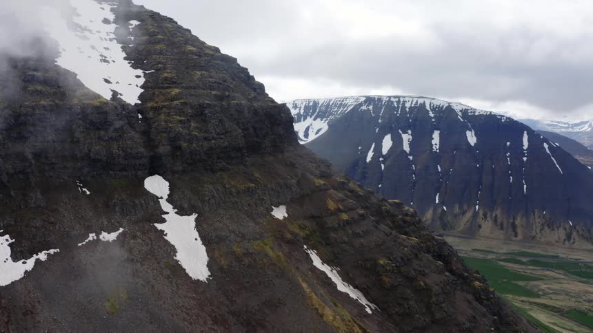 The peak of the very tall mountain has grass at its base