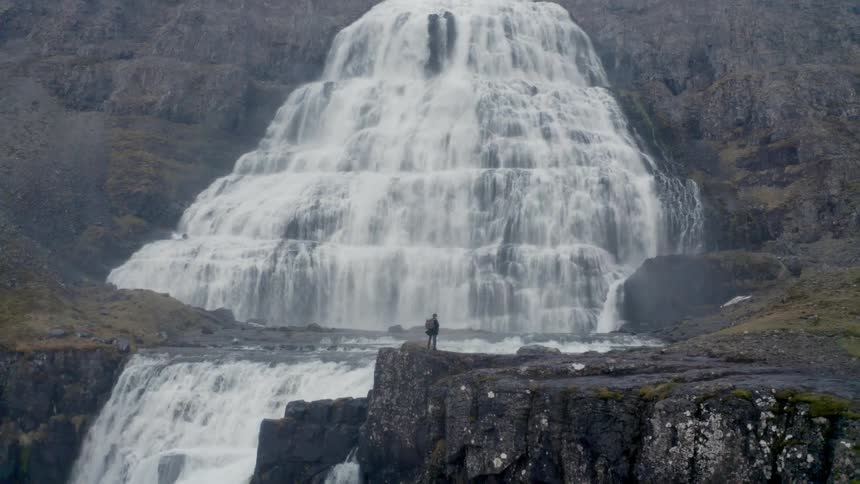 The man is standing in front of a large waterfall