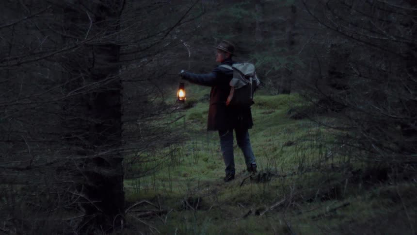 Hiker walking through the woods carrying a lantern and looking around