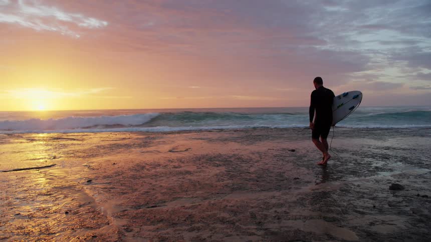 Surfer walking toward the sea during a colorful sunset
