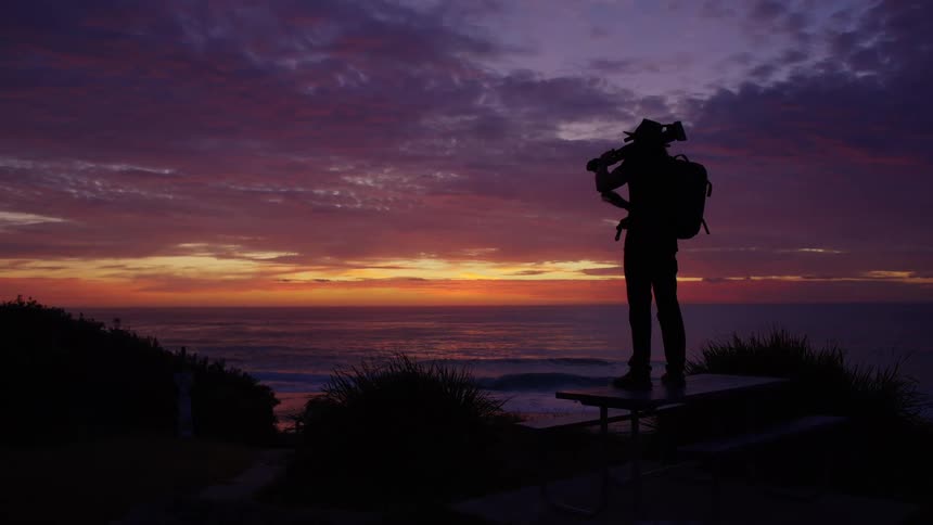 Person silhouetted on a picnic table watching the seaside sunset