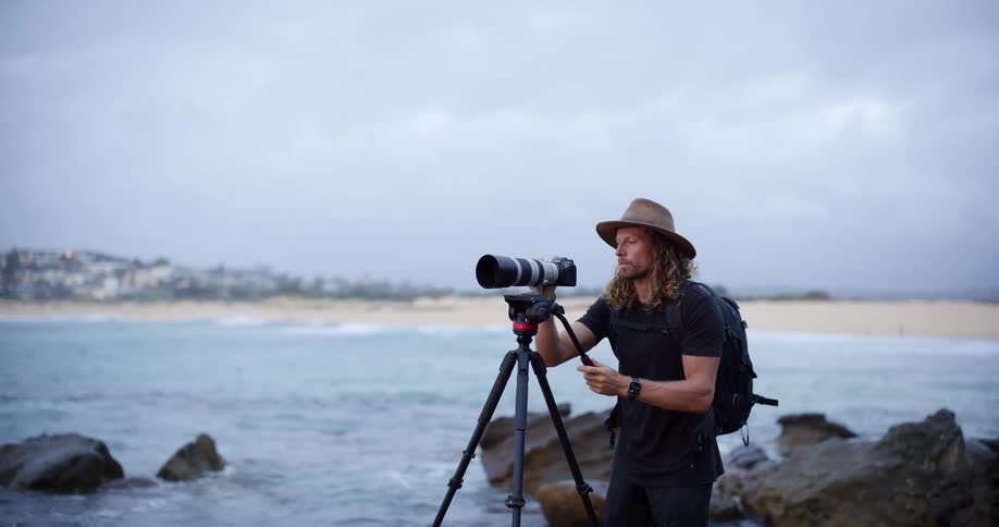 A man setting up a camera near some water
