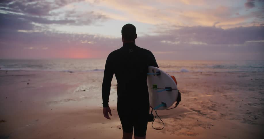 Surfer walking toward the ocean at sunrise