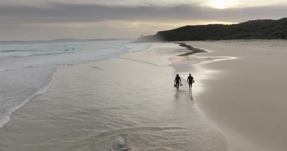 Two people walk along the beach sand at sunset with waves gently hitting the shoreline