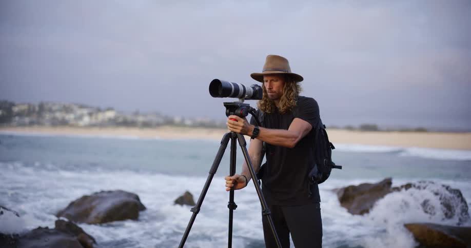 Photographer positioning a camera with a telephoto lens on a tripod atop coastal rocks