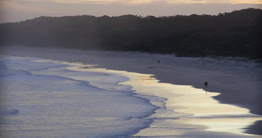 Calm gentle waves softly wash onto a reflective beach at dusk