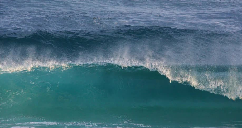 A tall wave rolls in and crashes mist drifting above the ocean surface