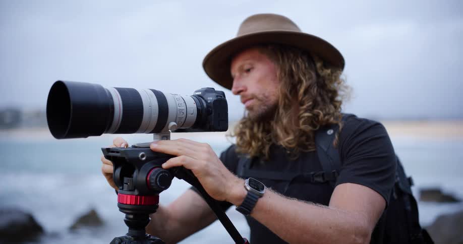 Photographer adjusting a camera with a telephoto lens mounted on a tripod by the seaside