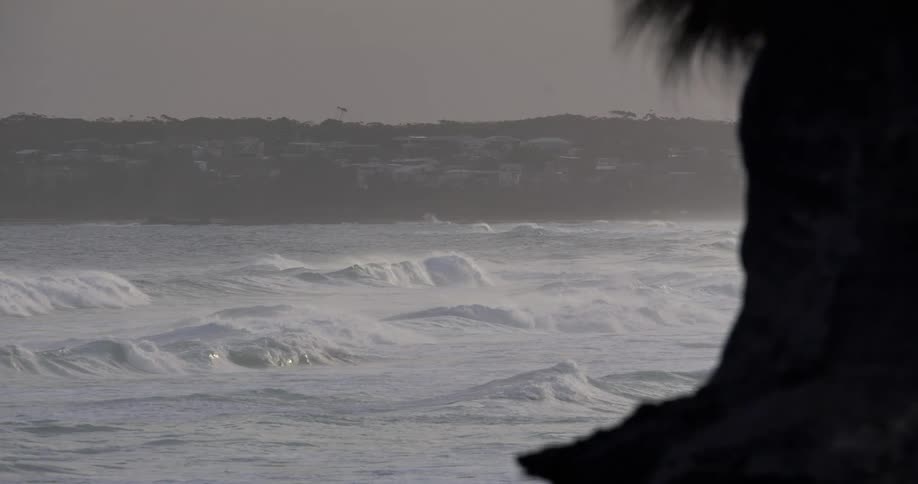 Strong waves breaking near the shore with a city in the background at dusk