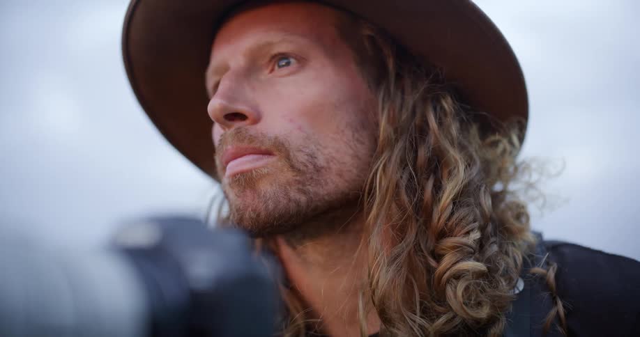 Man wearing a hat seen in closeup with a neutral expression outdoors