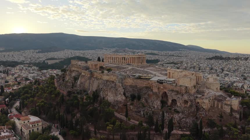 An aerial view captures the ancient acropolis rising above the sprawling city of athens as the sun sets over distant mountains