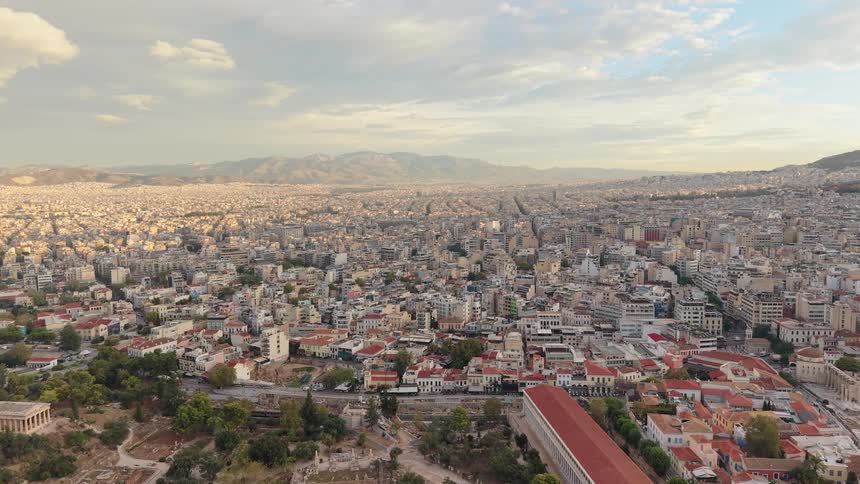 Aerial view of a sprawling city extending toward distant mountains with ancient ruins in the foreground