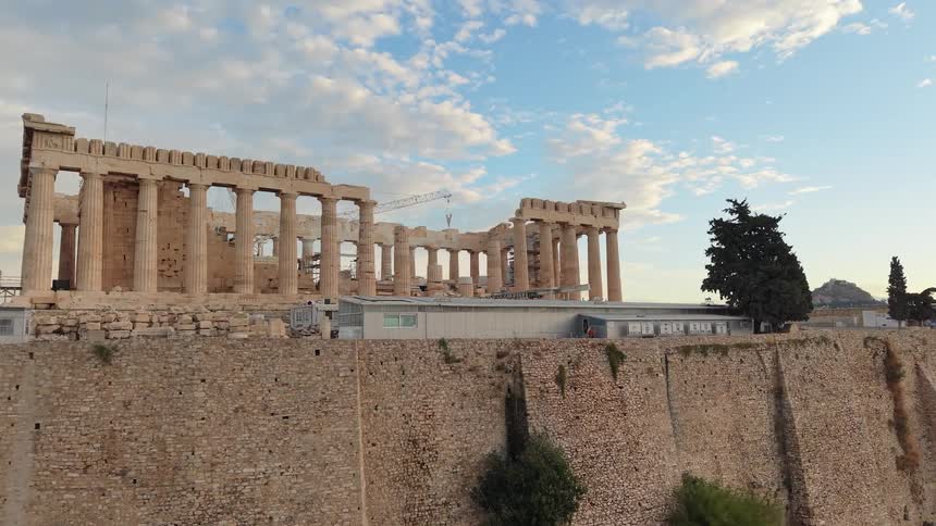 Frontal view of the parthenon with restoration structures around it under a partly cloudy sky