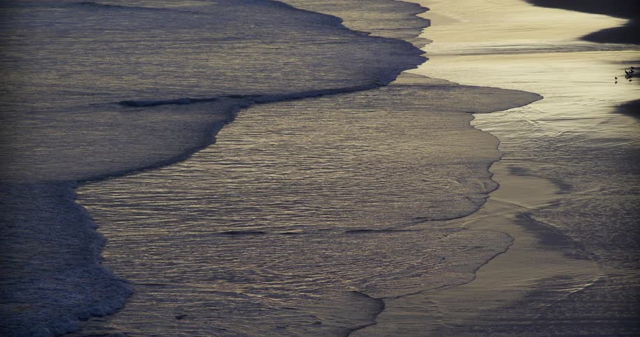 Gentle waves reaching a sandy shoreline lit by the low sun