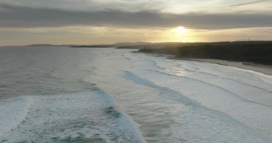 Waves roll in to shore and over the beach as the sun glows on the horizon