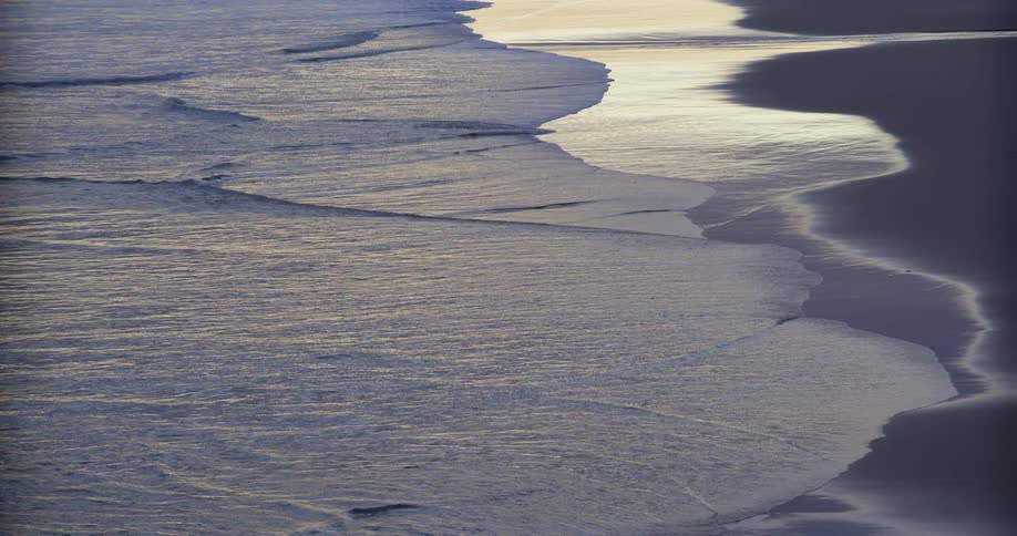 Waves roll in to shore and over the beach