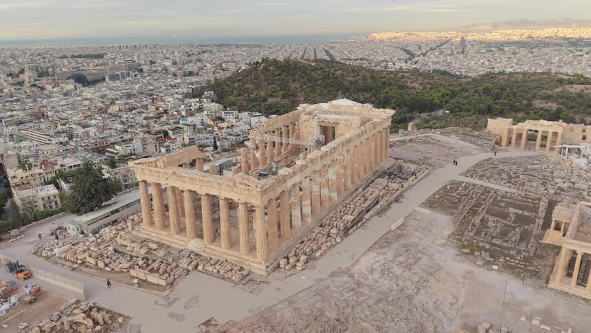 A temple on a hill lies in ruins with a city skyline in the background at midday