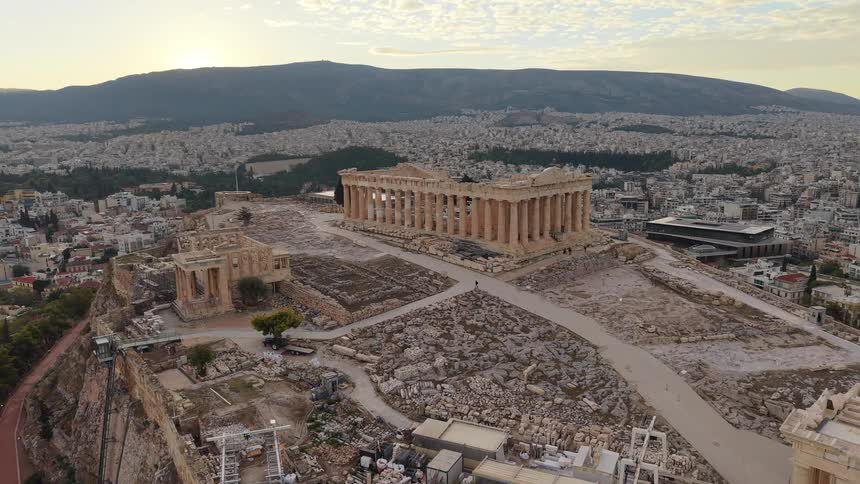 Aerial view of ancient ruins on a hilltop overlooking a sprawling modern city at sunrise