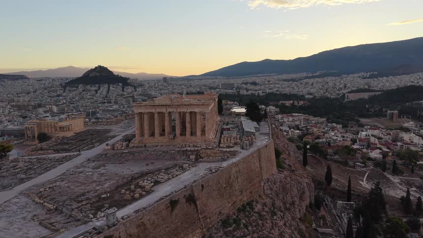Ancient ruins on top of a hill next to a city surrounded by mountains outdoors during dusk or dawn