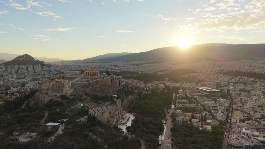 Aerial video captures a panoramic view of the acropolis of athens and the sprawling city set against a stunning sunrise or sunsetthe ancient ruins and surrounding urban landscape are highlighted by the bright low sun which casts a golden glow over th