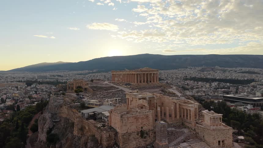 An aerial view captures the acropolis overlooking the sprawling city of athens as the sun dips behind the mountains